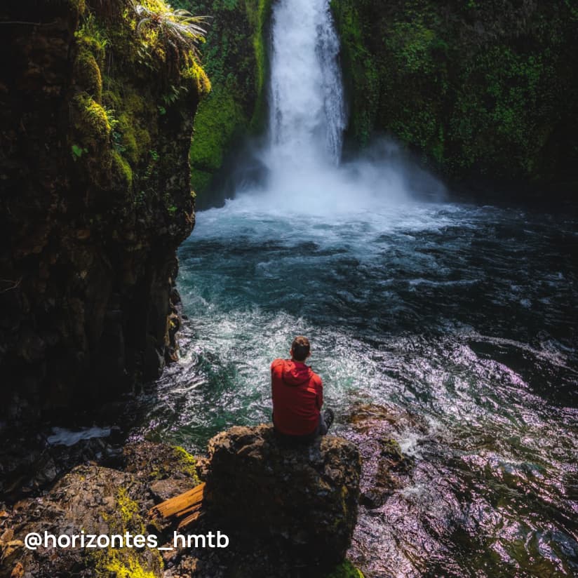 A person sitting on a rock and looking at a waterfall